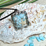 Quadratischer Larimar-Mosaik Anhänger im Edelstahlrahmen mit Seestern-Element und facettierter Bergkristall-Perle, eingebettet in Harz, an schwarzer Lederkette.