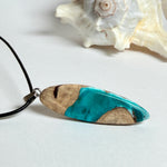 Handgefertigte Surfbrett Kette aus Maserholz und türkisfarbenem Resin mit Edelstahl Anhängerschlaufe an schwarzer Lederkette mit Karabiner und Verlängerung. Filigraner Ocean Anhänger inspiriert von Meer und Wellen, natürlicher Unikat Schmuck für Damen und Herren.