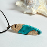 Handgefertigte Surfbrett Kette aus Maserholz und türkisfarbenem Resin mit Edelstahl Anhängerschlaufe an schwarzer Lederkette mit Karabiner und Verlängerung. Filigraner Ocean Anhänger inspiriert von Meer und Wellen, natürlicher Unikat Schmuck für Damen und Herren.