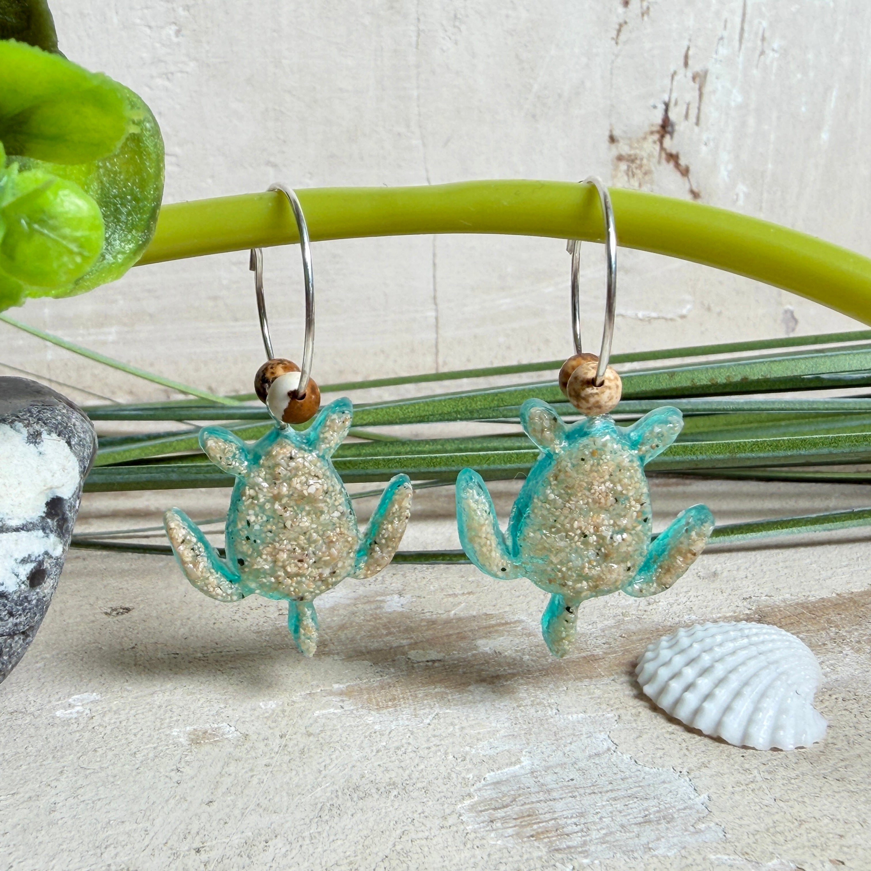 Türkisfarbene Schildkröten-Creolen an feinen 16-mm-Ringen aus 925 Silber, jeweils mit echtem Strandsand im Harz eingebettet und mit kleinen Jaspis-Edelsteinperlen verziert; handgefertigtes Unikat mit sommerlich-maritimem Look, fotografiert als Freisteller, Nahaufnahme oder auf dekorativem Untergrund.