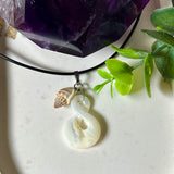 Detailaufnahme eines handgefertigten Anhängers aus echtem Perlmutt in Schlaufenform, kombiniert mit einer kleinen echten Muschel als Charm-Anhänger. Der Schmuck hängt an einer feinen schwarzen Lederschnur mit Edelstahlverschluss und symbolisiert Harmonie und Unendlichkeit. Ideal für Meeresliebhaberinnen und Fans von Naturmaterialien.