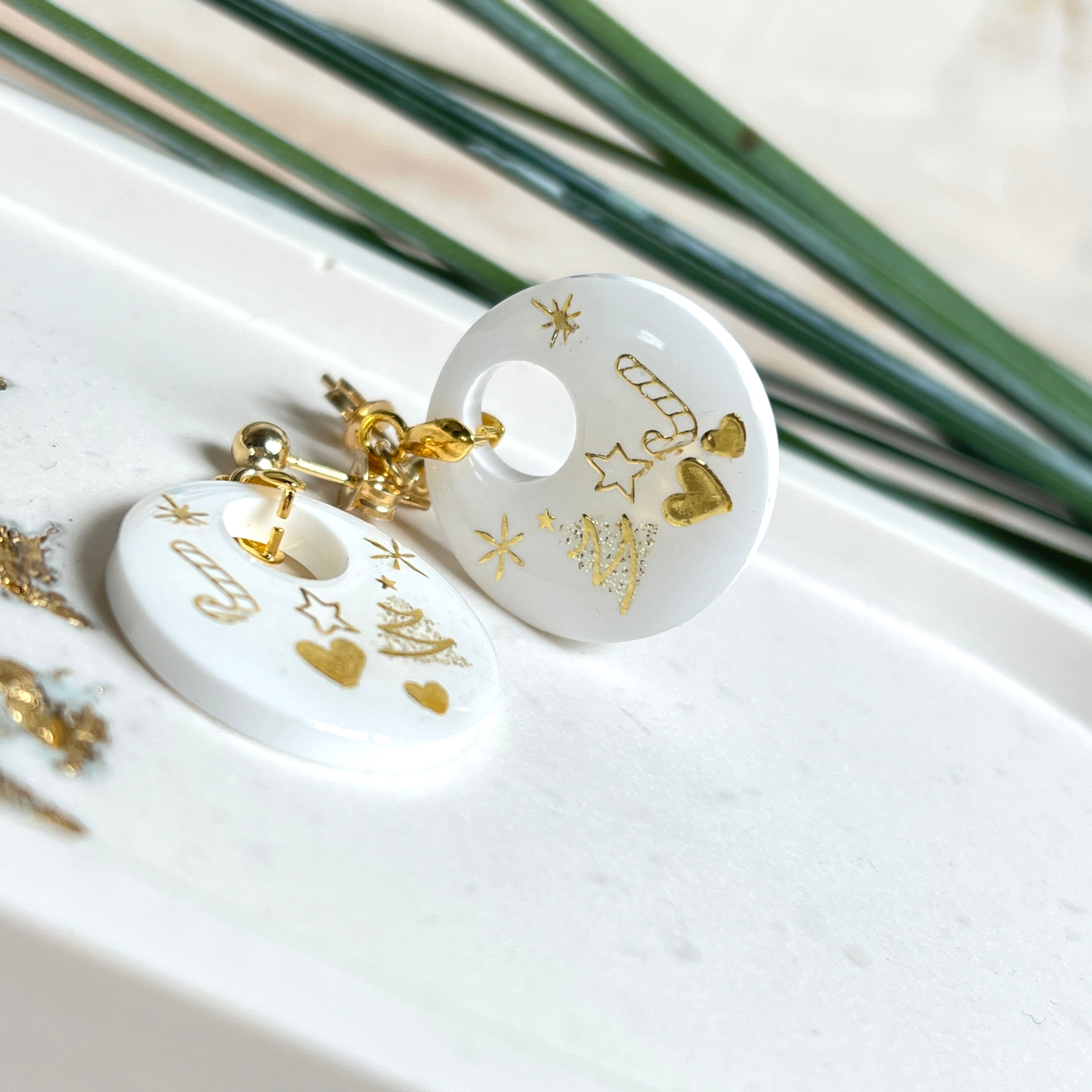 Handgefertigte Ohrringe aus weißem und klarem Harz mit goldenen Weihnachtsmotiven – Sterne, Herzen, Tannenbaum und Zuckerstange. Ohrstecker aus 925 Silber vergoldet, Anhängerschlaufe vergoldet. Größe ca. 37 mm × 25 mm. Leichte, elegante Festtagsohrringe mit warmem Goldglanz und winterlicher Ausstrahlung.