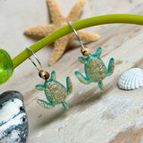 Türkisfarbene Schildkröten-Creolen an feinen 16-mm-Ringen aus 925 Silber, jeweils mit echtem Strandsand im Harz eingebettet und mit kleinen Jaspis-Edelsteinperlen verziert; handgefertigtes Unikat mit sommerlich-maritimem Look, fotografiert als Freisteller, Nahaufnahme oder auf dekorativem Untergrund.