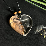 „Handgefertigter Herzanhänger aus Olivenholz und klarem Harz mit echter Pusteblume. Der Anhänger (ca. 3,5 × 3,5 cm) hängt an einem verstellbaren Lederband (23–43 cm) mit Holzperlen. Symbol für Wünsche und Glück, sorgfältig in Handarbeit gegossen, gesägt, geschliffen und poliert. Ein einzigartiger, naturinspirierter Anhänger – ideal als Geschenk oder persönlicher Talisman.“