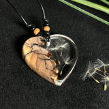 „Handgefertigter Herzanhänger aus Olivenholz und klarem Harz mit echter Pusteblume. Der Anhänger (ca. 3,5 × 3,5 cm) hängt an einem verstellbaren Lederband (23–43 cm) mit Holzperlen. Symbol für Wünsche und Glück, sorgfältig in Handarbeit gegossen, gesägt, geschliffen und poliert. Ein einzigartiger, naturinspirierter Anhänger – ideal als Geschenk oder persönlicher Talisman.“