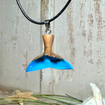 Handgefertigter Walflossen-Anhänger aus Olivenholz und Epoxidharz in Blau-Grün-Weiß, polierte Oberfläche, Edelstahl-Öse. Schwarze Lederkette 45 cm mit Edelstahl-Karabinerverschluss und 5 cm Edelstahl-Verlängerung. Anhängergröße ca. 2,5 × 3,2 cm, maritime Produktfotografie.