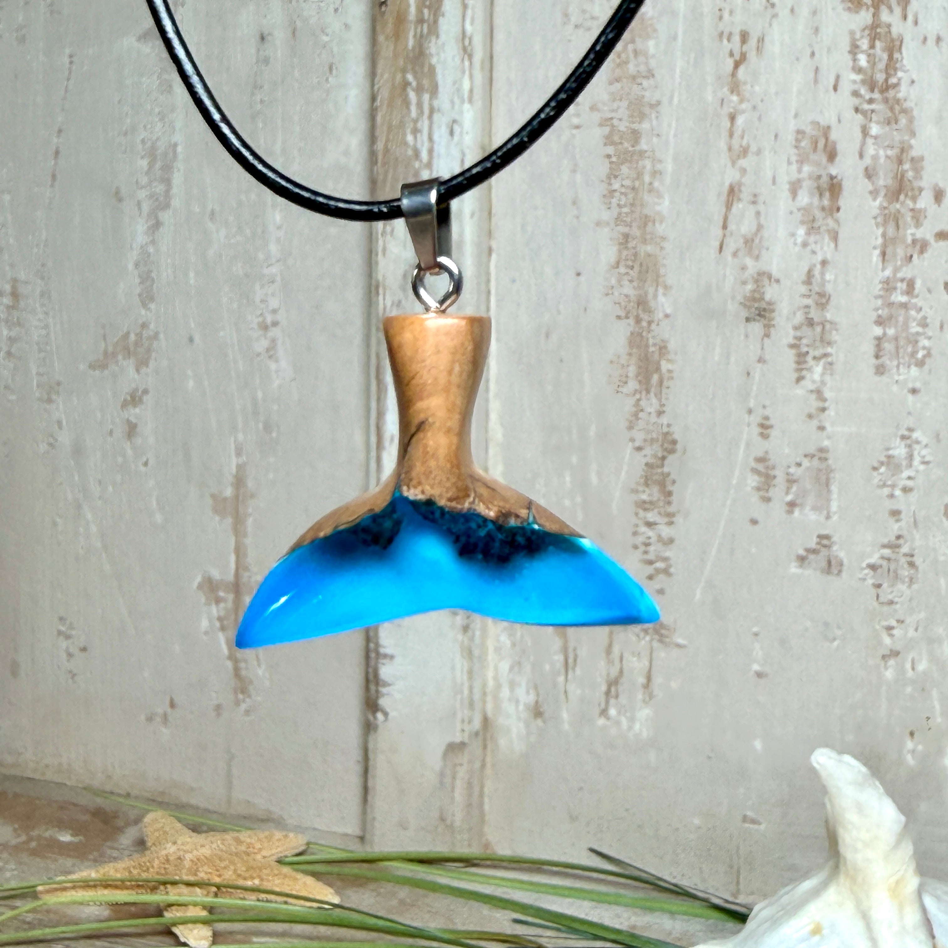 Handgefertigter Walflossen-Anhänger aus Olivenholz und Epoxidharz in Blau-Grün-Weiß, polierte Oberfläche, Edelstahl-Öse. Schwarze Lederkette 45 cm mit Edelstahl-Karabinerverschluss und 5 cm Edelstahl-Verlängerung. Anhängergröße ca. 2,5 × 3,2 cm, maritime Produktfotografie.