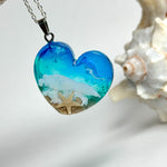 Ein herzförmiger Anhänger mit einer ganzen Ozeanwelt darin: Welle, Sand und Seestern in leuchtendem Blau und Türkis – handgegossen, einzigartig, unvergesslich. Mit versilberter Kette (46 cm) und Edelstahl-Karabiner.