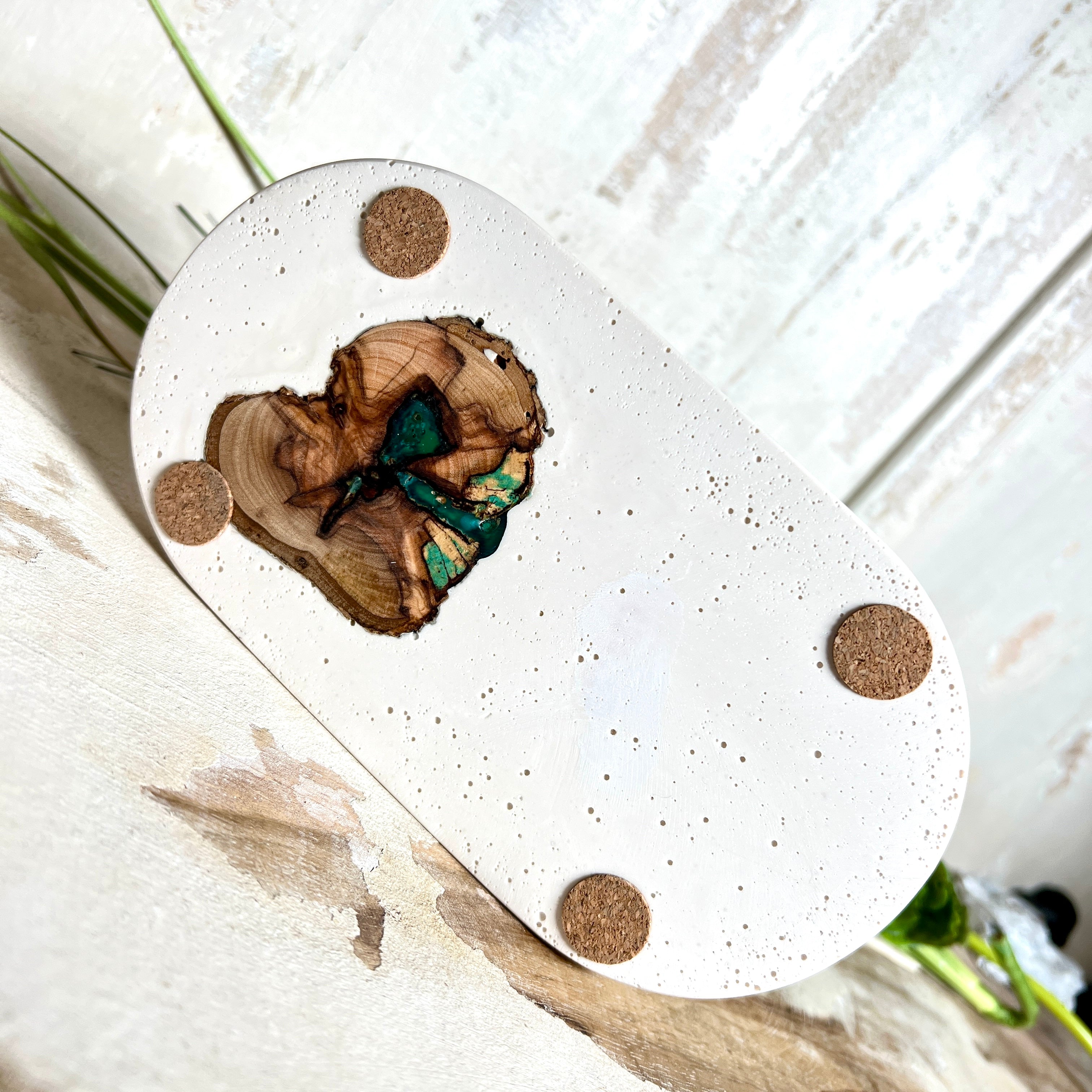 Handgefertigtes Schmucktablett aus Jesmonite mit eingebettetem Olivenholz und türkisfarbenem Resin. Die glänzende Oberfläche erinnert an Wasserstrukturen, während das Naturholz Tiefe und Wärme verleiht. Die Rückseite ist mit Korkpunkten versehen und schützt empfindliche Oberflächen. Perfekt als Ablage für Schmuck, Brille, Schlüssel oder Deko jedes Stück ein Unikat.