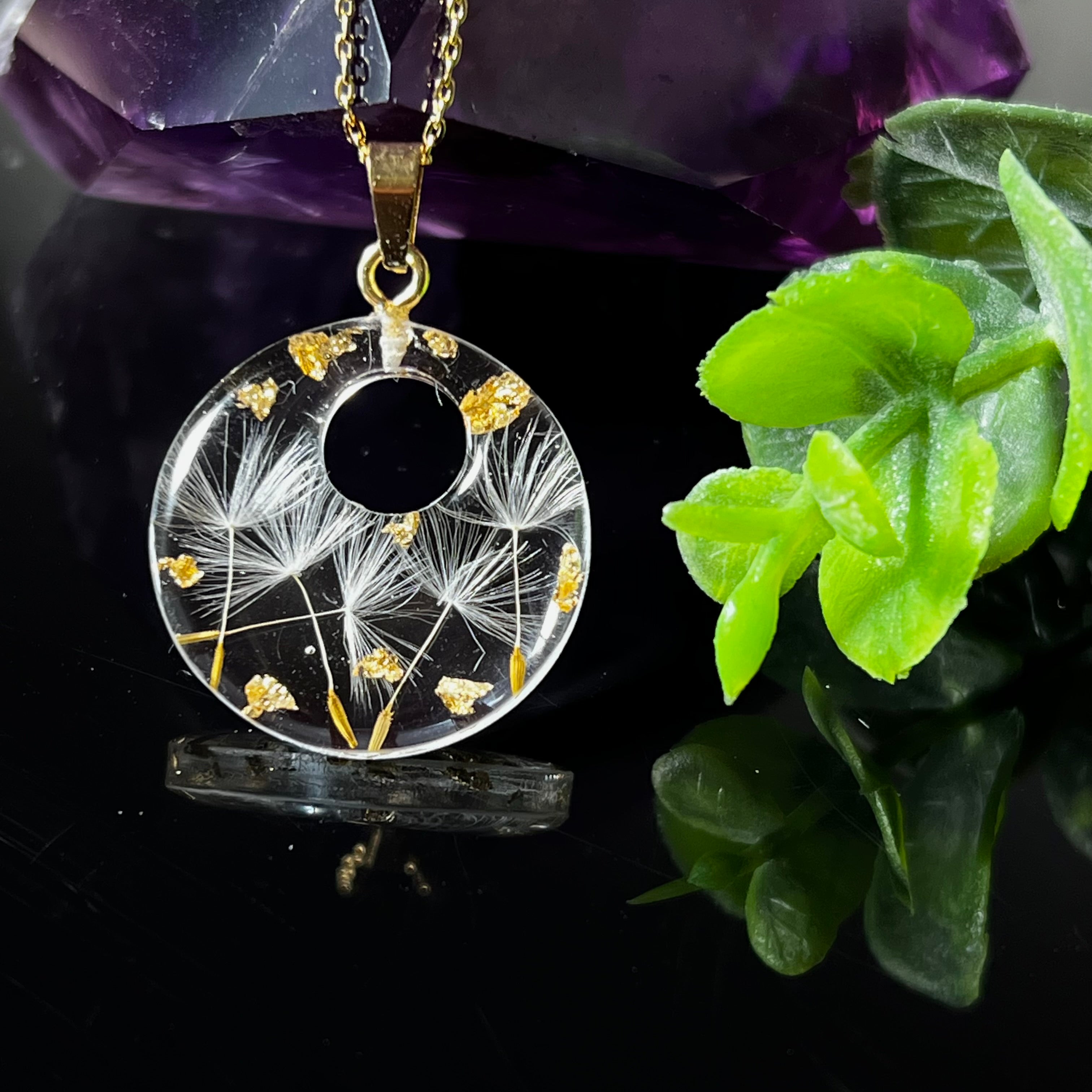 Runder Harzanhänger mit echten Pusteblumensamen und zarten Blattgold-Akzenten auf einer vergoldeten 925 Silberkette, 45 cm lang. Der Anhänger hat einen Durchmesser von ca. 2,6 cm und wird von einer goldfarbenen Edelstahlöse gehalten. Das Design symbolisiert Leichtigkeit, Hoffnung und Naturverbundenheit – perfekt als Geschenk oder für Naturliebhaberinnen. Liebevoll von Hand gefertigt und ein echtes Unikat.
