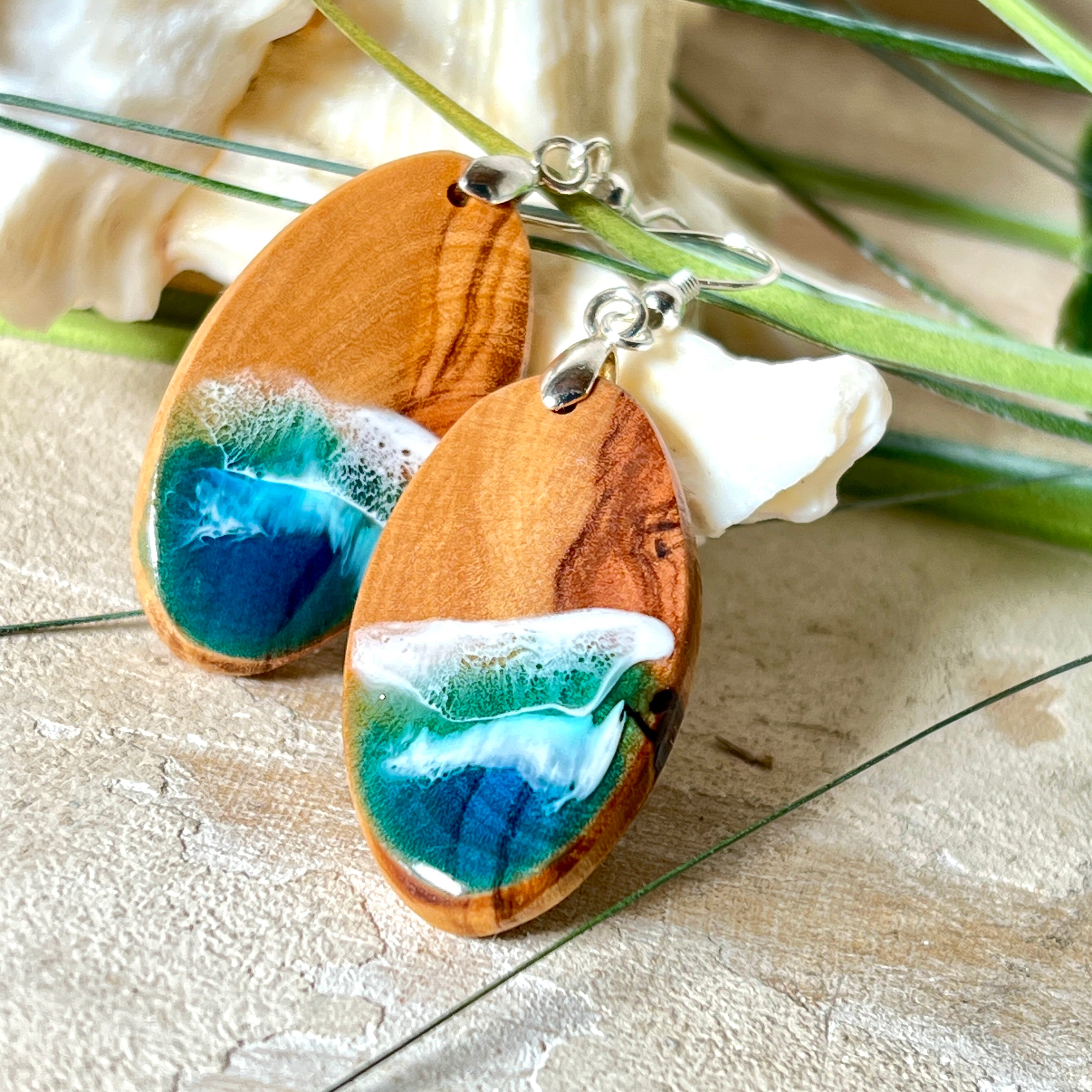Handgefertigte Ohrringe „Wave Harmony“ aus Olivenholz und Epoxidharz in Blau-, Türkis- und Weißtönen. Das Design erinnert an Meereswellen am Strand. Jeder Ohrring ist ein Unikat mit individueller Maserung. Versilberte, nickelfreie und bleifreie Anhängerschlaufe, 925 Silber Ohrhaken. Maritimer Schmuck – perfekt für Meerliebhaber und als edles Geschenk.