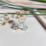 Kleiner Bärchen-Anhänger aus transparentem Harz mit irisierenden Flakes in Regenbogen-Schimmer, goldfarbene Anhängerschlaufe aus Edelstahl. Größe ca. 2,2 × 2,1 cm. Handgefertigtes Unikat; Flakes-Anordnung variiert, vereinzelt kleine Luftbläschen möglich.