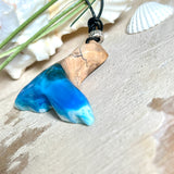 Handgefertigter Walflossen-Anhänger aus Olivenholz und glänzendem Harz in Blau-Grün-Weiß – maritimer Schmuck „Flossenklang“. Der Anhänger erinnert an die Form einer Walflosse und vereint die natürliche Maserung des Holzes mit dem schimmernden Farbspiel des Harzes. Mit verstellbarem schwarzen Lederband und Spacerperle. Ideal für Meeresliebhaber und Naturliebhaber – jedes Stück ein Unikat.