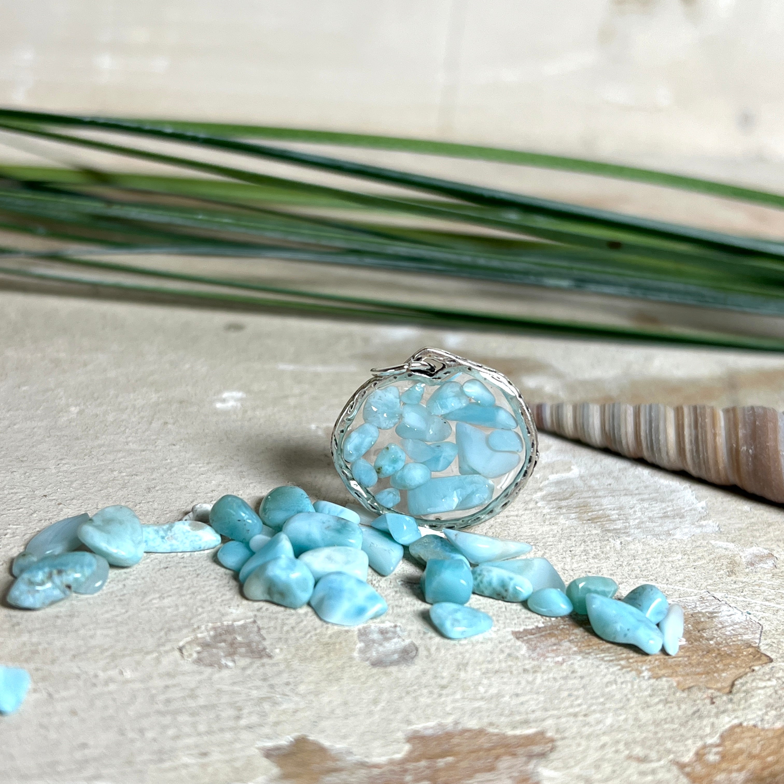 Runder Anhänger „Atlantis Dream“ aus antik-silberfarbener Zinklegierung, gefüllt mit kleinen Larimar-Edelsteinchen und klarem Resin. Die Larimarsteine zeigen sanfte Blau- und Weißtöne, die an das Meer erinnern. Durchmesser ca. 22 mm, handgefertigtes Unikat, fotografiert auf maritimem Untergrund mit kleinen Larimarsteinen und Muscheln zur Größenorientierung.