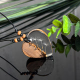 Handgefertigter Herzanhänger aus warm gemasertem Olivenholz und kristallklarem Epoxidharz mit schwebenden Pusteblumensamen. Schwarzes, verstellbares Lederband mit Schiebeknoten und naturfarbenen Holzperlen, Anhänger ca. 3,5 × 3,3 cm. Naturnaher Unikatschmuck von ZeitlosSchmuckDesign.