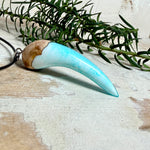 Handgefertigter Anhänger aus Edelholz und transparent-türkisblauem und weißen Epoxidharz, glatt poliert. Größe ca. 6,5 × 2,0 cm. Mit Edelstahlöse an schwarzer Lederkette (45 cm + 5 cm Edelstahl-Verlängerung, Karabiner). Moderner, unisex tragbarer Schmuck mit natürlicher Holzmaserung; kleine Lufteinschlüsse sind charakteristisch.