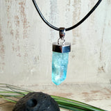 Nahaufnahme einer handgefertigten Halskette mit Aqua Aura Rohkristall: naturbelassener, sechskantiger Bergkristall mit goldbedampfter Aqua-Beschichtung in Türkisblau, gefasst in 925er Silber und getragen an einer schwarzen Lederkette mit Edelstahl-Karabiner und Verlängerungskettchen.