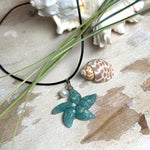 Seestern-Anhänger aus transparentem Harz mit echtem Meersand ( leicht eingefärbt), in blautürkis Strand-Look, mit kleiner Süßwasserperle als Anhänger-Detail. Edelstahlöse, schwarze Lederkette mit Edelstahl-Karabiner und Verlängerung (45 cm + 5 cm). Anhänger ca. 3,5 × 3,5 cm. Handgefertigtes Unikat; vereinzelt kleine Luftbläschen möglich, typisch für Handarbeit.