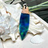Beidseitig tragbarer Surfbrett-Anhänger aus Olivenholz, kombiniert mit klaren Epoxidharz in Blau-Grün. Eingearbeiteter synthetischer Opal erzeugt ein faszinierendes Farbspiel wie Nordlichter. Größe ca. 6 × 1,8 cm. Mit verstellbarem Lederband (26–45 cm), dekorativen Perlen & Schiebeknoten. Handgefertigt & einzigartig. Ein Schmuckstück mit Naturinspiration.