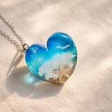 Ein herzförmiger Anhänger mit einer ganzen Ozeanwelt darin: Welle, Sand und Seestern in leuchtendem Blau und Türkis – handgegossen, einzigartig, unvergesslich. Mit versilberter Kette (46 cm) und Edelstahl-Karabiner.
