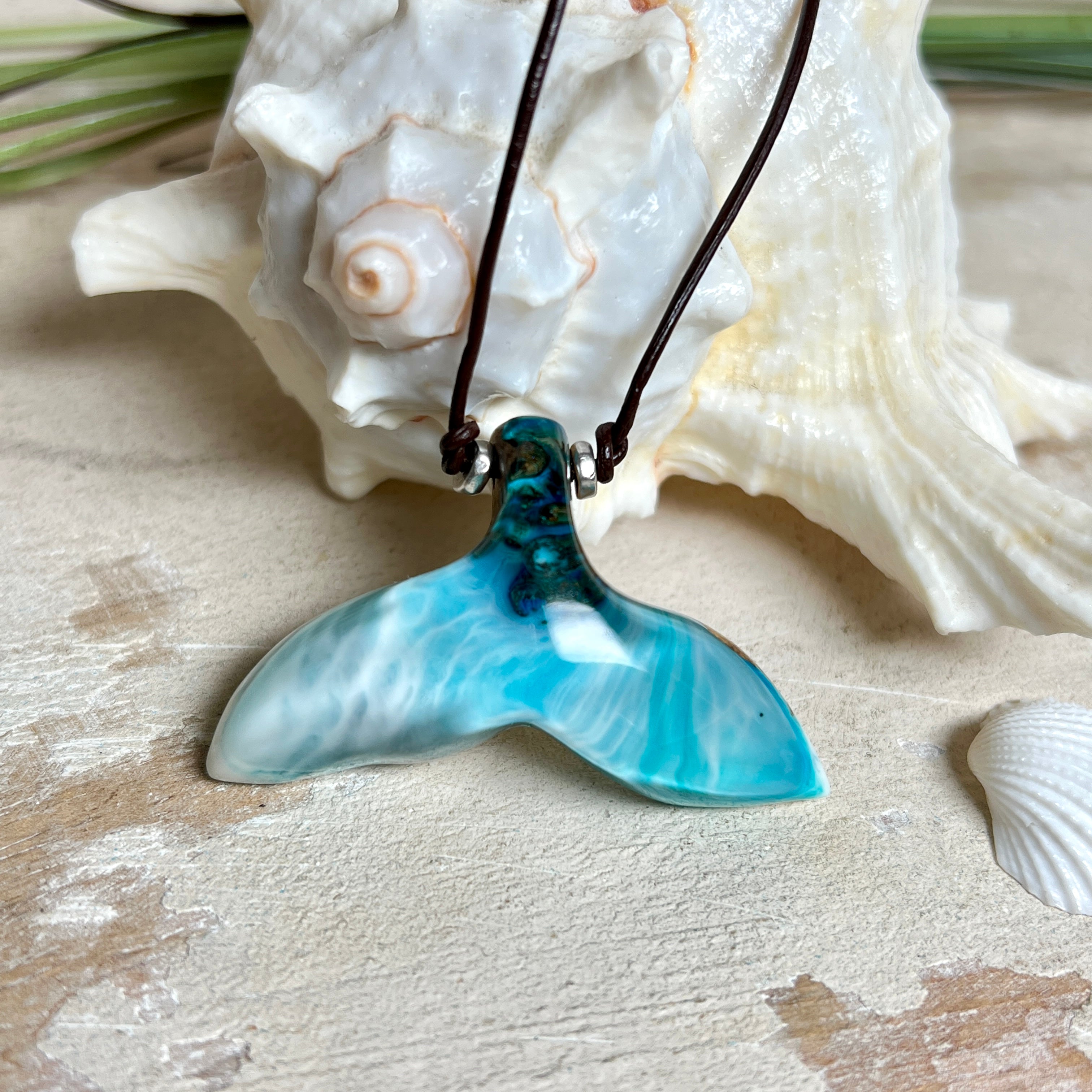 Walflossen-Anhänger „Flossenklang“ – handgefertigtes Unikat aus Maserholz und türkis-blau-grauen und weißem Harz. Die elegant geschwungene Form erinnert an die Flosse eines Wals und symbolisiert Freiheit, Stärke und Naturverbundenheit. Mit verstellbarem braunem Lederband gefertigt, ist jedes Stück ein individuelles Schmuckstück für Meeresliebhaber und Natursuchende. Maritimer Halsschmuck, inspiriert vom Ozean, glatt poliert und mit Liebe zum Detail von Hand gearbeitet.