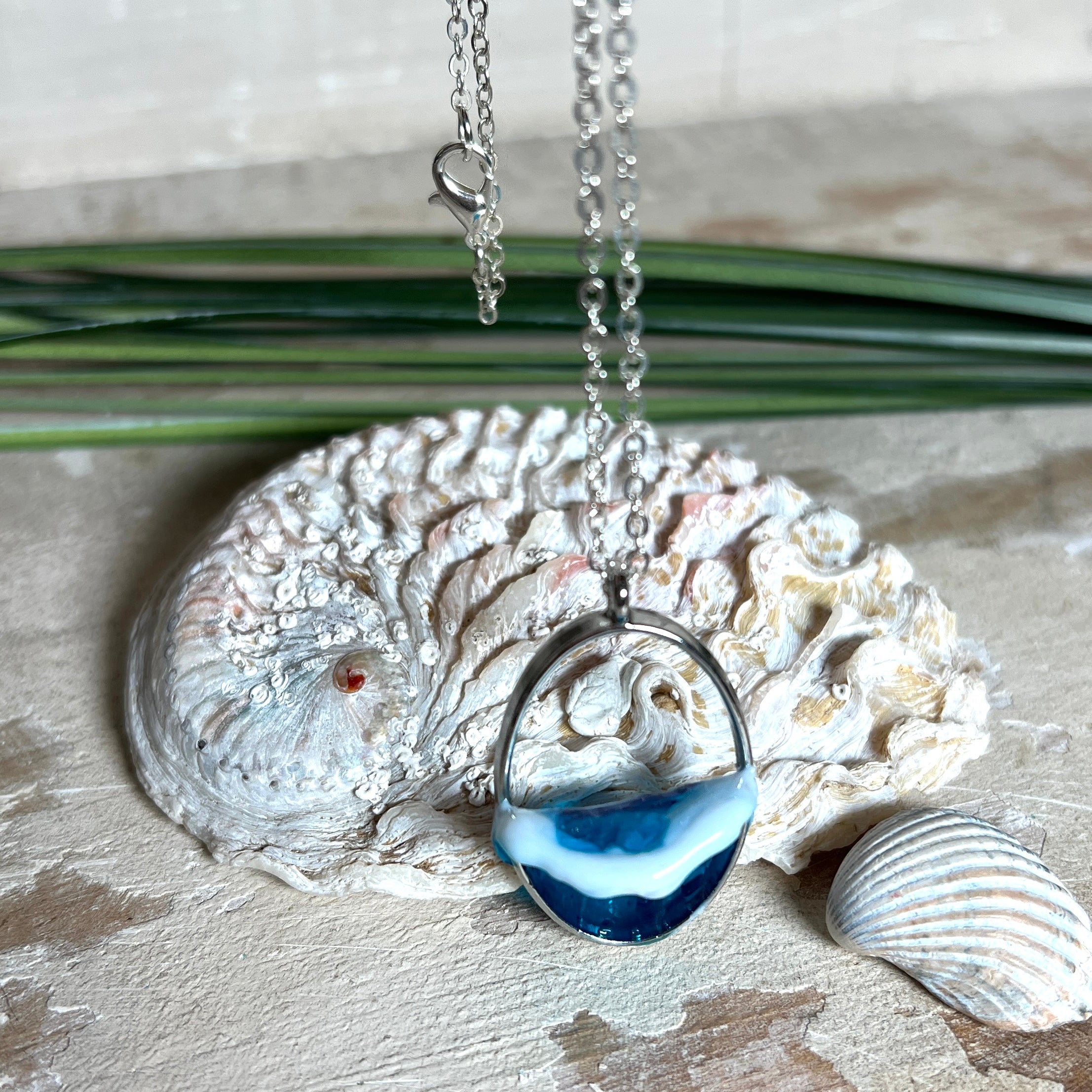 Ovale Halskette „Ocean Crest“ mit 3D-Welle: handgefertigter Harz-Anhänger in Silber-Legierung, Farbverlauf von Tiefblau zu Türkis mit weißer Schaumkrone. Größe ca. 3,9 × 2,3 cm, an einer ca. 56 cm langen versilberten Kette. Glänzende Oberfläche, maritimer Look, Unikat-Handarbeit.