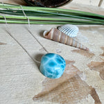 Feine Kette mit rundem Larimar-Cabochon in AA-Qualität. Der ca. 20 mm große Stein zeigt ein intensives Blau mit hellen, netzartigen Zeichnungen und ist mittig mit einer 2,5 mm Bohrung versehen, durch die eine zarte 925 Silberkette (45 cm, ca. 1 mm stark) geführt wird. 