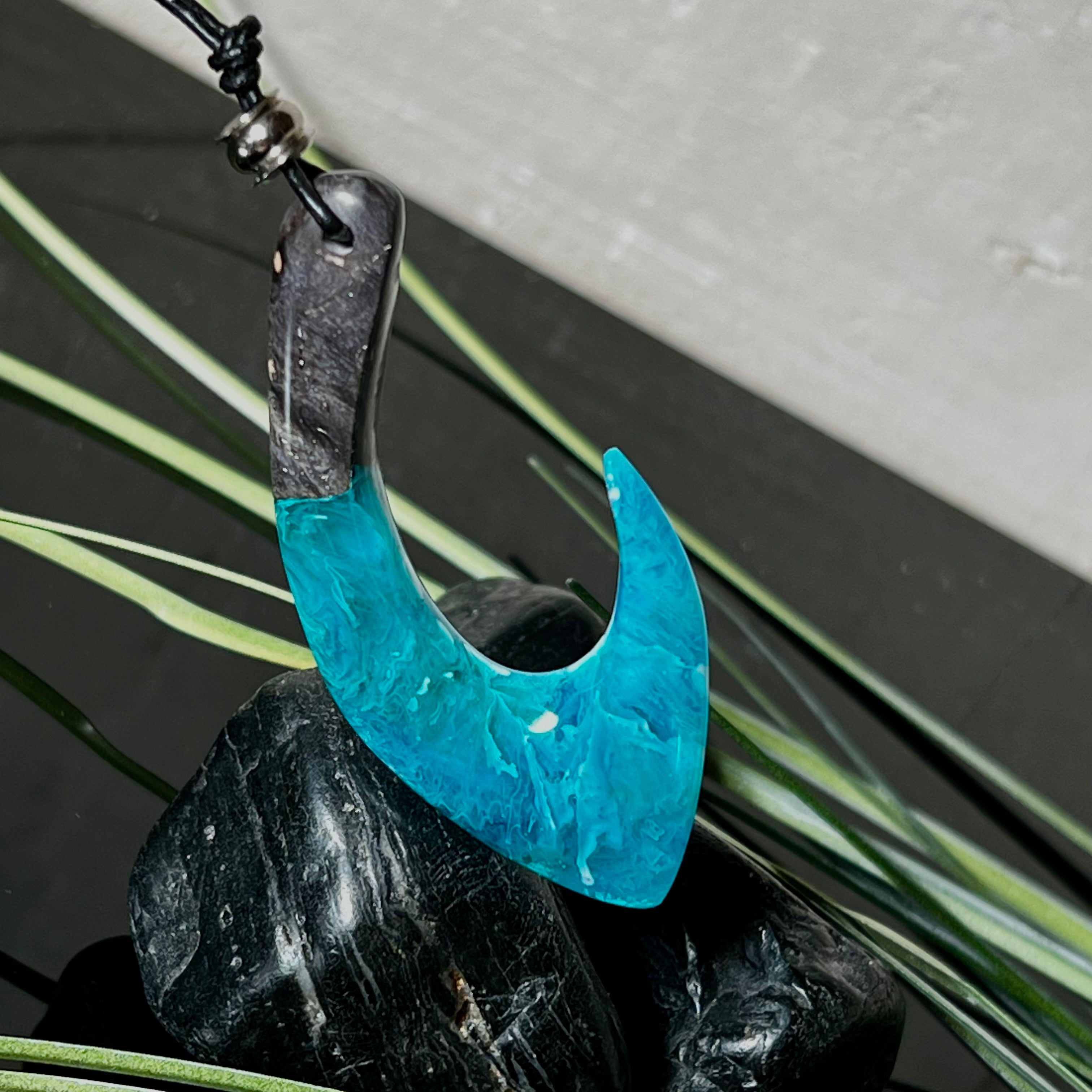 Handgefertigter Maori-Anhänger „Tangaroa Spirit“ in traditioneller Hakenform, gefertigt aus stabilisiertem Maserholz und ozeanblauem Harz. Die polierte Oberfläche bringt die natürlichen Maserungen und das tiefblaue Farbspiel besonders zur Geltung. Symbolisiert Schutz, Stärke und die Verbundenheit zum Meer. Verstellbares Lederband mit Schiebeknoten und dekorativen Holz- sowie Metallperlen – ideal als kraftvoller Talisman oder Geschenk.
