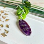 Ovaler Anhänger mit echter Pusteblume in Harz, Hintergrund Brombeerfarben. Größe 4 × 1,8 cm, versilberte Kette 50 cm mit Karabinerverschluss. Handgefertigtes Unikat.