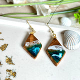 Handgefertigte Ohrringe „Ocean Diamond“ aus Olivenholz und Epoxidharz in Diamantform. Türkis-, Blau- und Weißtöne bilden ein wellenartiges Design, inspiriert vom Meer. Jeder Ohrring ist ein Unikat mit individueller Maserung. Vergoldete, nickelfreie und bleifreie Anhängerschlaufe, 925 Sterling Silber Ohrhaken. Maritimer Schmuck für Meerliebhaber und besondere Anlässe.