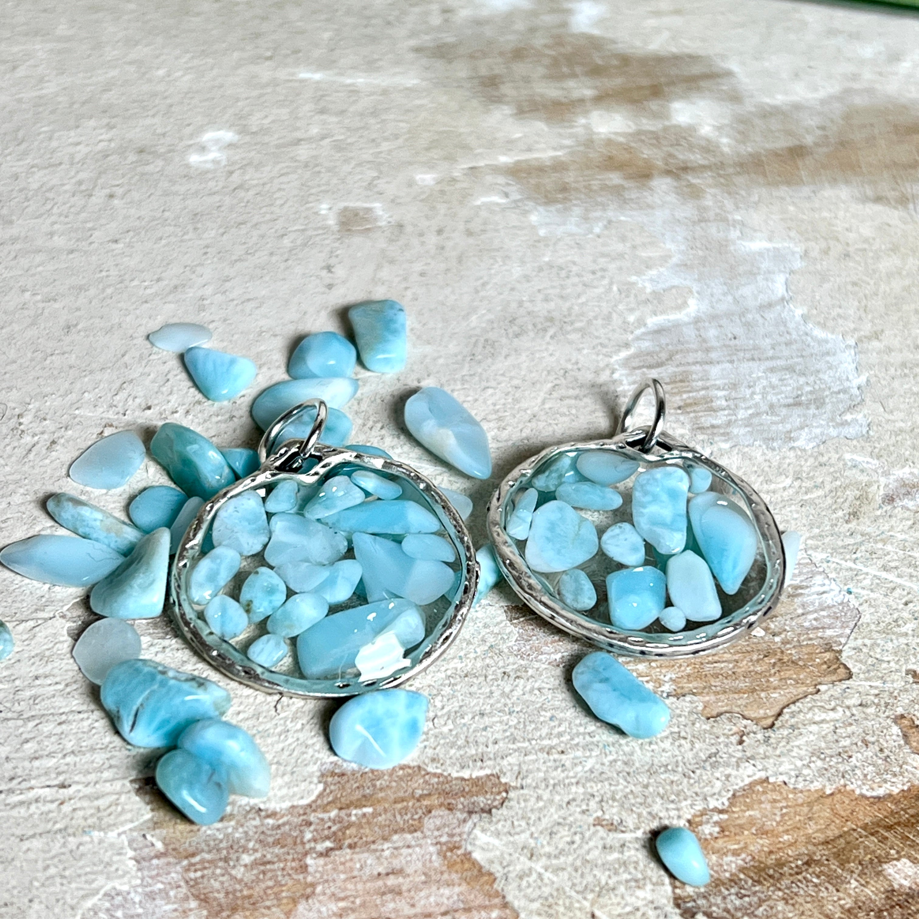 Runder Anhänger „Atlantis Dream“ aus antik-silberfarbener Zinklegierung, gefüllt mit kleinen Larimar-Edelsteinchen und klarem Resin. Die Larimarsteine zeigen sanfte Blau- und Weißtöne, die an das Meer erinnern. Durchmesser ca. 22 mm, handgefertigtes Unikat, fotografiert auf maritimem Untergrund mit kleinen Larimarsteinen und Muscheln zur Größenorientierung.