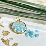 Runder Anhänger „Golden Atlantis Dream“ mit kleinen Larimar-Edelsteinchen in klarem Resin, gefasst in einer 24K vergoldeten Zinklegierung in Shiny Gold. Die Larimarsteine zeigen sanfte Blau- und Weißtöne wie karibische Wellen. Durchmesser ca. 22 mm, handgefertigtes Unikat, fotografiert mit Larimarsteinchen, Muscheln und einer 2-Euro-Münze zur Größenorientierung auf maritimem Untergrund.