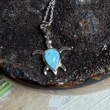 Feine Schildkröten-Kette aus rhodiniertem 925 Silber. Im Panzer des Anhängers liegt ein tropfenförmiger Larimar in hellem Blau. Der Anhänger ist ca. 22 x 18 mm groß und hängt an einer 45 cm langen, 1 mm starken Silberkette.