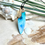 Surfbrett-Anhänger handgefertigt aus Maserholz & Harz in Blau-Weiß. Größe ca. 6,3 × 2 cm. Lederband verstellbar 26–47 cm, Schiebeknoten mit Holzperlen.