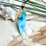 Surfbrett-Anhänger handgefertigt aus Maserholz & Harz in Blau-Weiß. Größe ca. 6,3 × 2 cm. Lederband verstellbar 26–47 cm, Schiebeknoten mit Holzperlen.