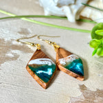 Handgefertigte Ohrringe „Ocean Diamond“ aus Olivenholz und Epoxidharz in Diamantform. Türkis-, Blau- und Weißtöne bilden ein wellenartiges Design, inspiriert vom Meer. Jeder Ohrring ist ein Unikat mit individueller Maserung. Vergoldete, nickelfreie und bleifreie Anhängerschlaufe, 925 Sterling Silber Ohrhaken. Maritimer Schmuck für Meerliebhaber und besondere Anlässe.