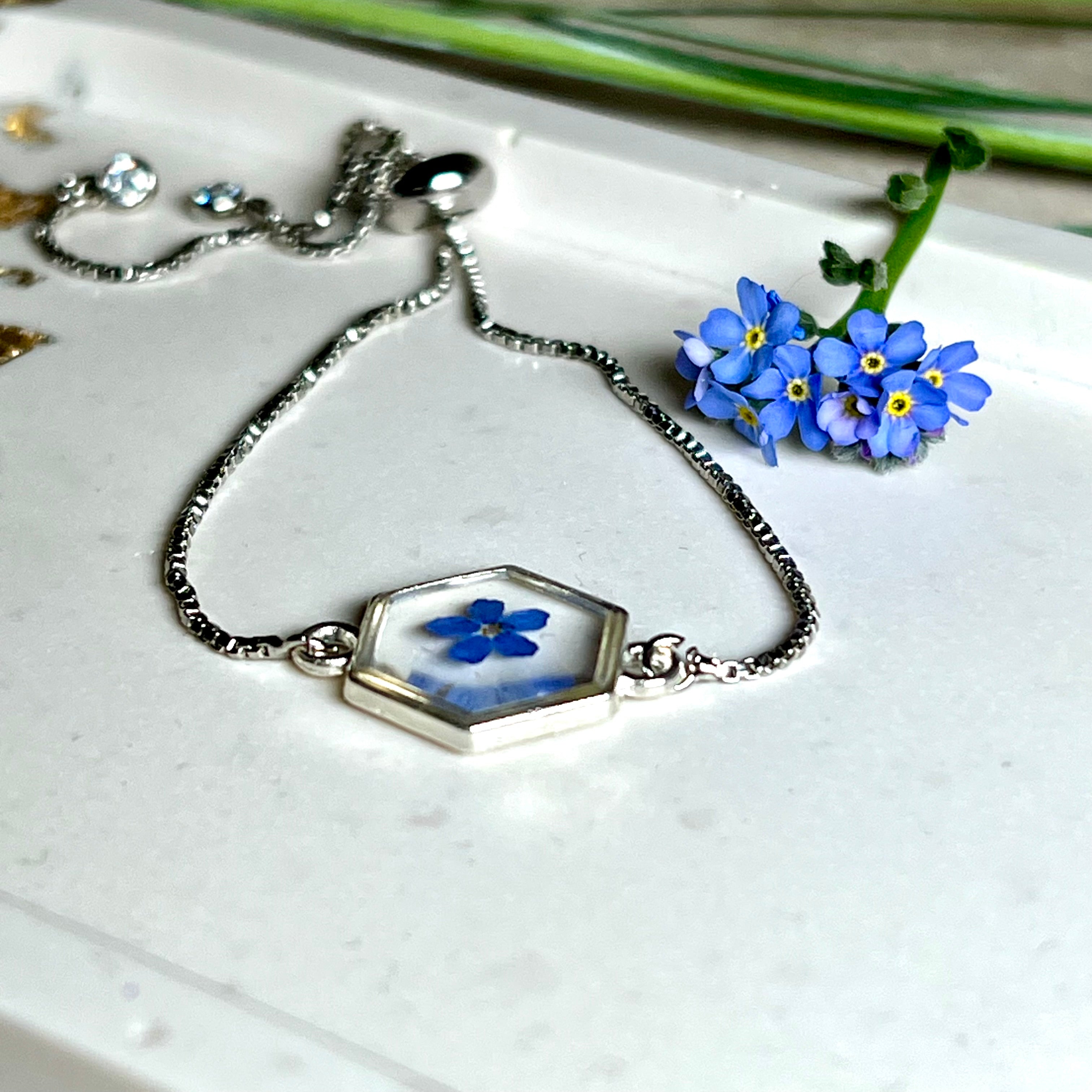 „Handgefertigtes Armband mit echter Vergissmeinnicht-Blume, eingebettet in klares Harz. Verstellbares Edelstahlarmband mit Schiebeverschluss und funkelnden Zirkonia-Endperlen. Symbolträchtiger Schmuck für Frauen – ideal als Geschenk zum Muttertag, Geburtstag oder zur Erinnerung an einen besonderen Menschen.“
