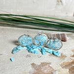 Runder Anhänger „Atlantis Dream“ aus antik-silberfarbener Zinklegierung, gefüllt mit kleinen Larimar-Edelsteinchen und klarem Resin. Die Larimarsteine zeigen sanfte Blau- und Weißtöne, die an das Meer erinnern. Durchmesser ca. 22 mm, handgefertigtes Unikat, fotografiert auf maritimem Untergrund mit kleinen Larimarsteinen und Muscheln zur Größenorientierung.