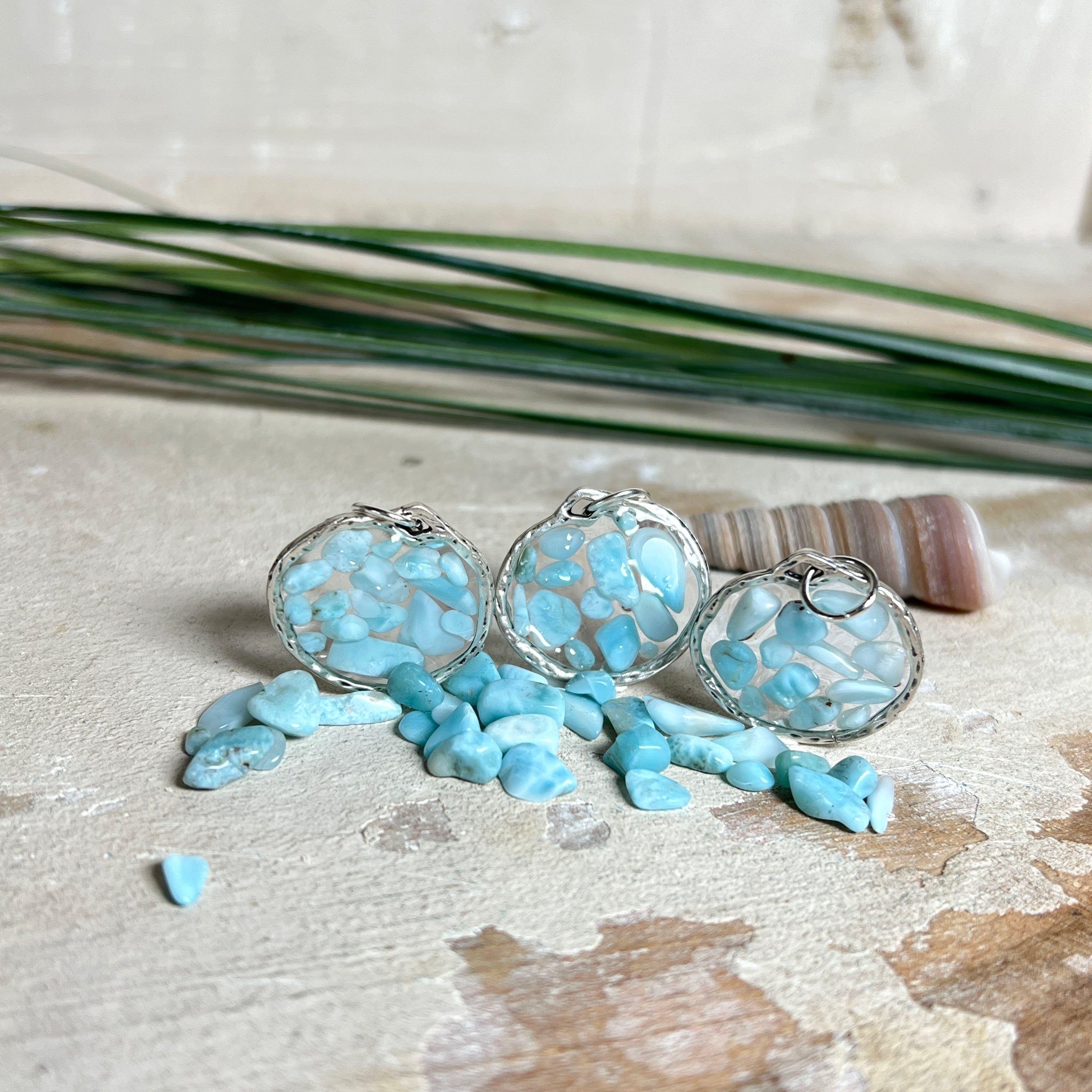 Runder Anhänger „Atlantis Dream“ aus antik-silberfarbener Zinklegierung, gefüllt mit kleinen Larimar-Edelsteinchen und klarem Resin. Die Larimarsteine zeigen sanfte Blau- und Weißtöne, die an das Meer erinnern. Durchmesser ca. 22 mm, handgefertigtes Unikat, fotografiert auf maritimem Untergrund mit kleinen Larimarsteinen und Muscheln zur Größenorientierung.