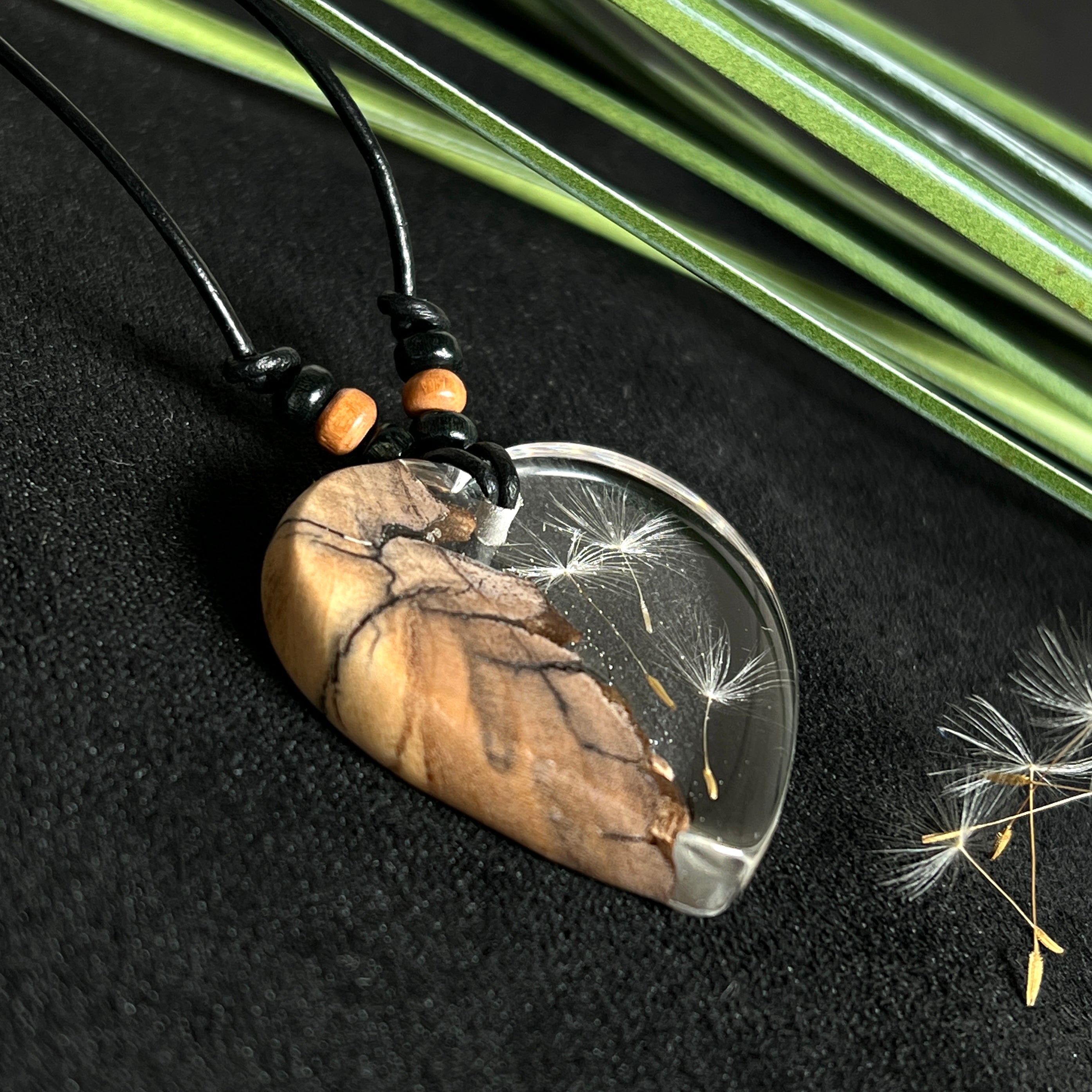 „Handgefertigter Herzanhänger aus Olivenholz und klarem Harz mit echter Pusteblume. Der Anhänger (ca. 3,5 × 3,5 cm) hängt an einem verstellbaren Lederband (23–43 cm) mit Holzperlen. Symbol für Wünsche und Glück, sorgfältig in Handarbeit gegossen, gesägt, geschliffen und poliert. Ein einzigartiger, naturinspirierter Anhänger – ideal als Geschenk oder persönlicher Talisman.“