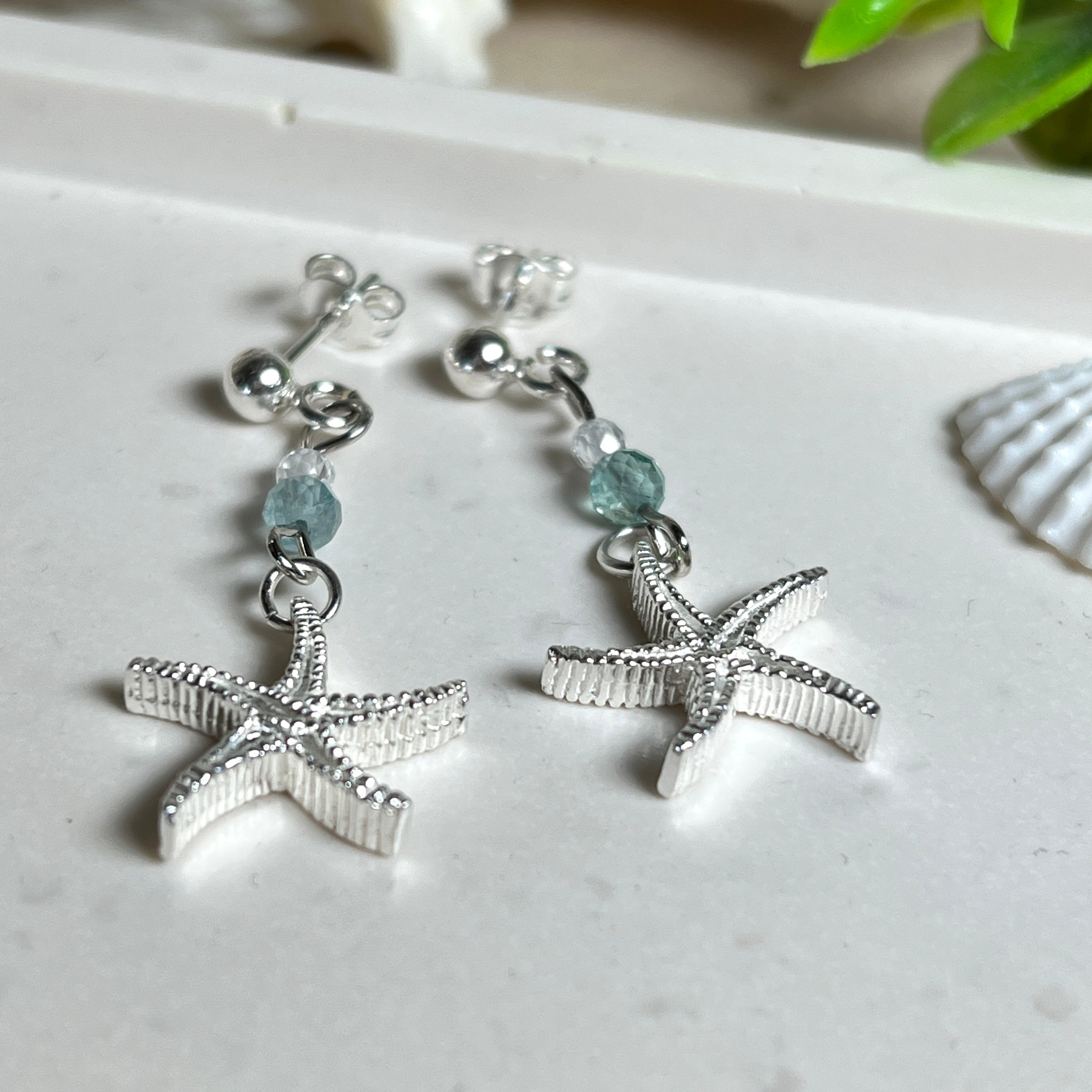 Edle „Ocean Star“ Ohrringe aus 925 Sterling Silber mit Seestern-Anhängern (18 × 17 mm), verziert mit einer aquablauen Apatitperle und funkelndem Zirkonia. Länge getragen: 45 mm. Maritime Schmuckstücke, die das Funkeln des Meeres einfangen – elegant, hochwertig und ein ideales Geschenk für Meeresliebhaber und Sommerträume.