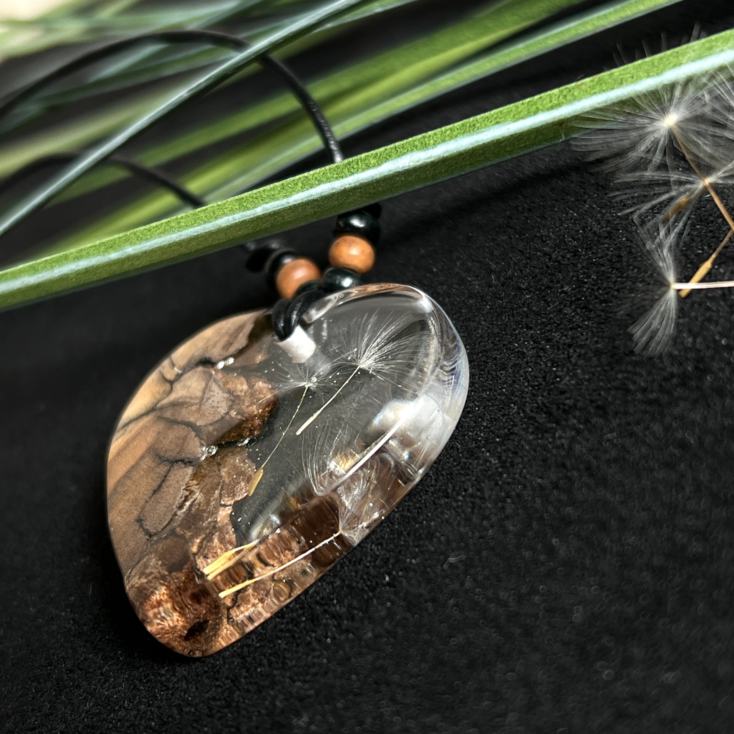 „Handgefertigter Herzanhänger aus Olivenholz und klarem Harz mit echter Pusteblume. Der Anhänger (ca. 3,5 × 3,5 cm) hängt an einem verstellbaren Lederband (23–43 cm) mit Holzperlen. Symbol für Wünsche und Glück, sorgfältig in Handarbeit gegossen, gesägt, geschliffen und poliert. Ein einzigartiger, naturinspirierter Anhänger – ideal als Geschenk oder persönlicher Talisman.“