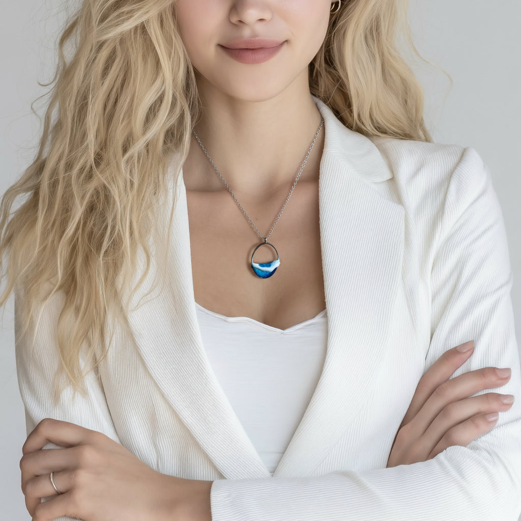 Ovale Halskette „Ocean Crest“ mit 3D-Welle: handgefertigter Harz-Anhänger in Silber-Legierung, Farbverlauf von Tiefblau zu Türkis mit weißer Schaumkrone. Größe ca. 3,9 × 2,3 cm, an einer ca. 56 cm langen versilberten Kette. Glänzende Oberfläche, maritimer Look, Unikat-Handarbeit.