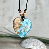 Handgefertigter Herzanhänger aus Maserholz und transparentem Ocean-Harz mit echtem Seestern und Muscheln. Die zarten Aqua-Farben erinnern an Meereswellen. Lederband verstellbar mit Holzperlen. Größe ca. 3,5 × 3,2 cm. Natürliches, maritimes Unikat von ZeitlosSchmuckDesign