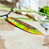 Handgefertigte Halskette „Tropical Glow“ mit Surfbrett-Anhänger aus naturbelassenem Rebholz (Weinrebe) und marmoriertem Epoxidharz in Grün, Orange, Türkis und Weiß. Größe des Anhängers ca. 6,5 × 2 cm. Das Harz fluoresziert eindrucksvoll unter UV-/Schwarzlicht. Edelstahl-Anhängerschlaufe, schwarze Lederkette (45 cm + 5 cm Verlängerung) mit Edelstahl-Karabiner. Unikat in maritim-sommerlichem Stil, ideal als besonderes Geschenk.