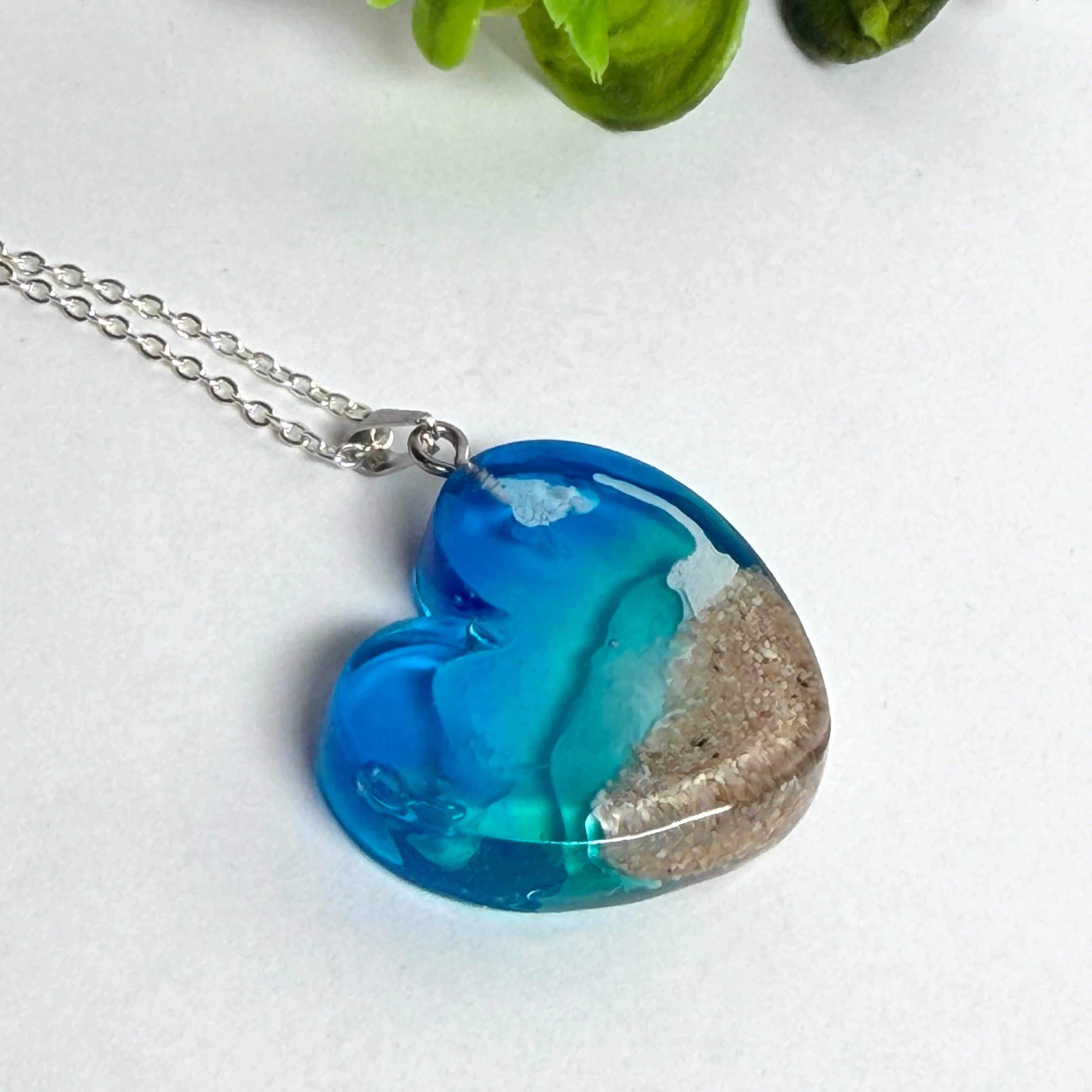 Ein herzförmiger Anhänger mit einer ganzen Ozeanwelt darin: Welle, Sand und Seestern in leuchtendem Blau und Türkis – handgegossen, einzigartig, unvergesslich. Mit versilberter Kette (46 cm) und Edelstahl-Karabiner.