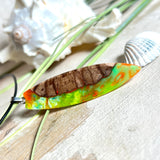 Handgefertigte Halskette „Tropical Glow“ mit Surfbrett-Anhänger aus naturbelassenem Rebholz (Weinrebe) und marmoriertem Epoxidharz in Grün, Orange, Türkis und Weiß. Größe des Anhängers ca. 6,5 × 2 cm. Das Harz fluoresziert eindrucksvoll unter UV-/Schwarzlicht. Edelstahl-Anhängerschlaufe, schwarze Lederkette (45 cm + 5 cm Verlängerung) mit Edelstahl-Karabiner. Unikat in maritim-sommerlichem Stil, ideal als besonderes Geschenk.