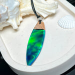 Beidseitig tragbarer Surfbrett-Anhänger aus Olivenholz, kombiniert mit klaren Epoxidharz in Blau-Grün. Eingearbeiteter synthetischer Opal erzeugt ein faszinierendes Farbspiel wie Nordlichter. Größe ca. 6 × 1,8 cm. Mit verstellbarem Lederband (26–45 cm), dekorativen Perlen & Schiebeknoten. Handgefertigt & einzigartig. Ein Schmuckstück mit Naturinspiration.