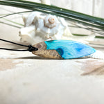 Surfbrett-Anhänger handgefertigt aus Maserholz & Harz in Blau-Weiß. Größe ca. 6,3 × 2 cm. Lederband verstellbar 26–47 cm, Schiebeknoten mit Holzperlen.