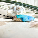 Surfbrett-Anhänger handgefertigt aus Maserholz & Harz in Blau-Weiß. Größe ca. 6,3 × 2 cm. Lederband verstellbar 26–47 cm, Schiebeknoten mit Holzperlen.